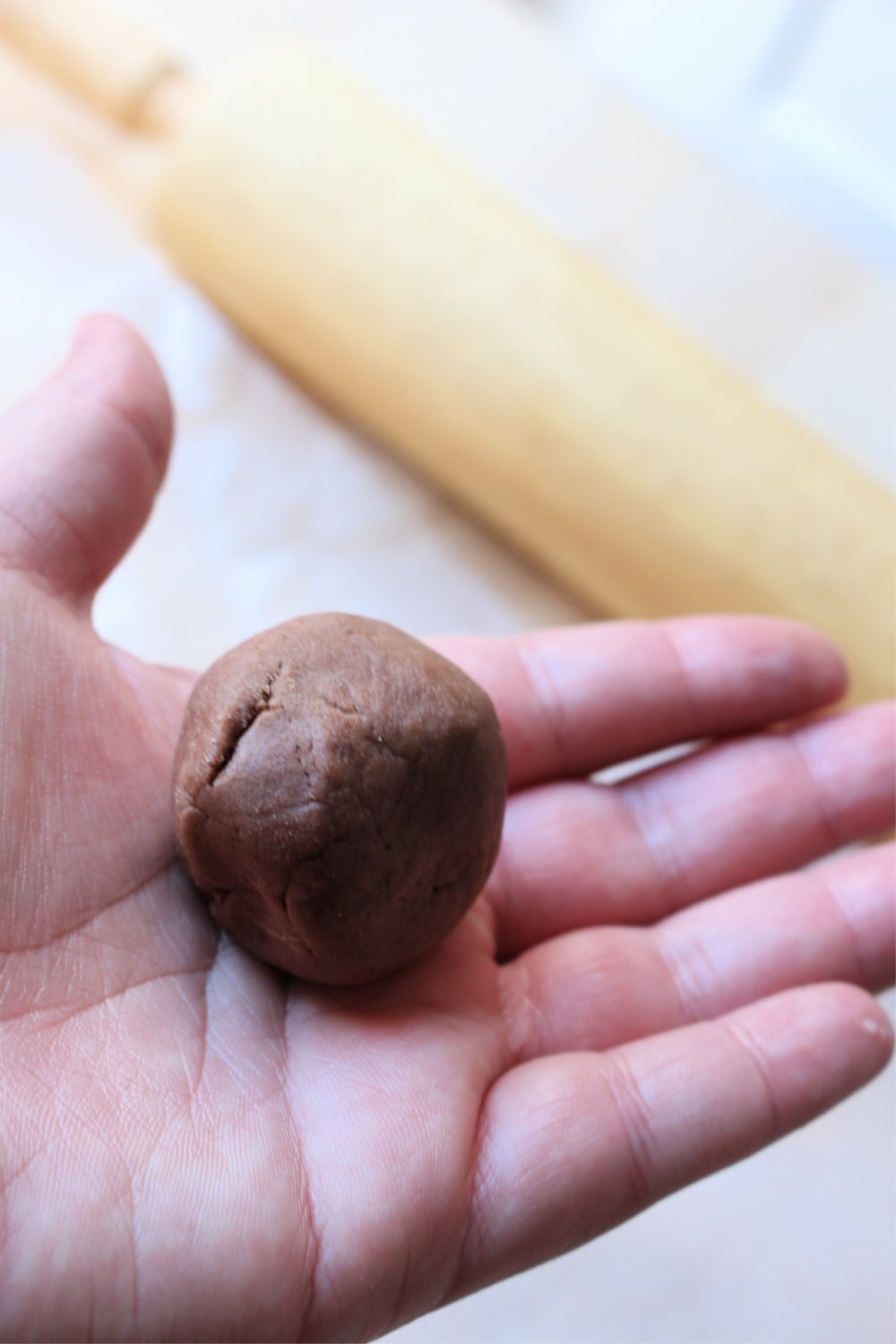 Hand holding ball of chocolate topping for conchas next to rolling pin.