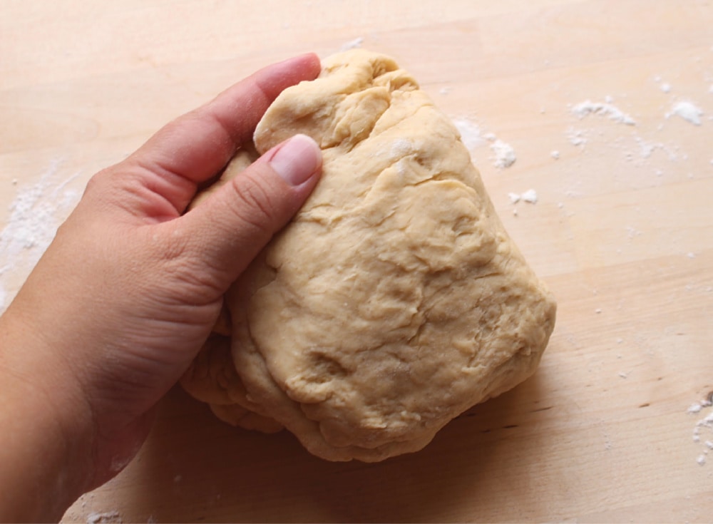 Hand kneading conchas dough on a wooden surface.