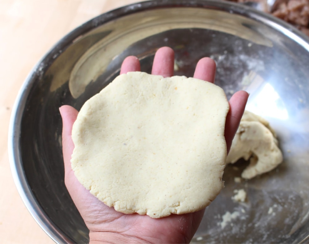 A hand covered in a tortilla-size of masa. 