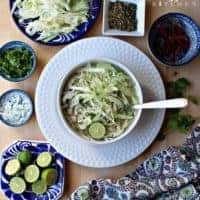 A white bowl of pozole blanco (or chicken pozole) surrounded by the toppings.