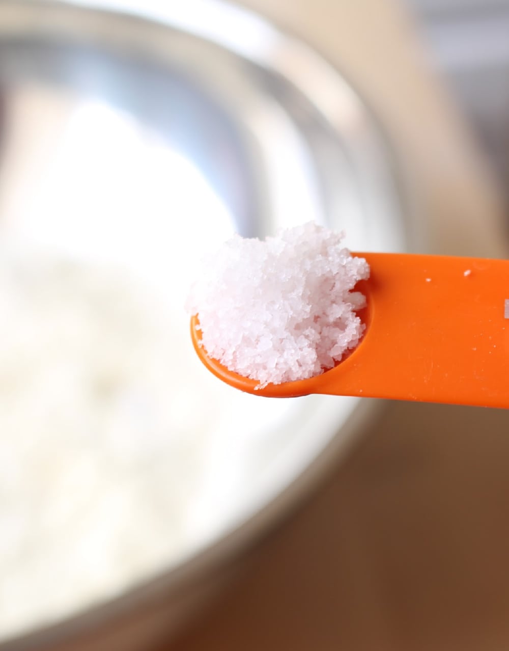 Orange measuring spoon with salt over a bowl of masa harina.