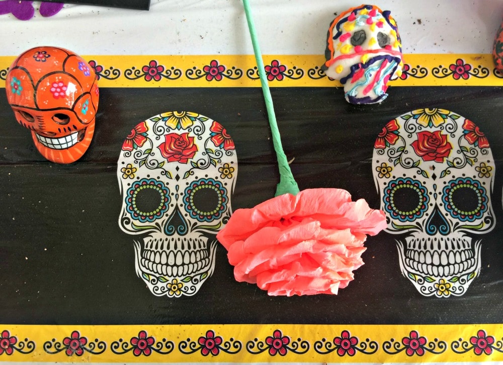 Skulls and paper flowers next to decorative Mexican skulls outline. 