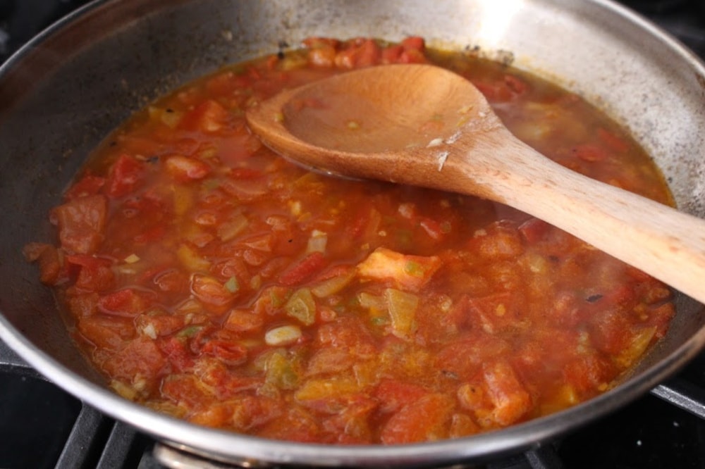 A skillet with cooked tomatoes and onions and a wooden spoon on the side. 