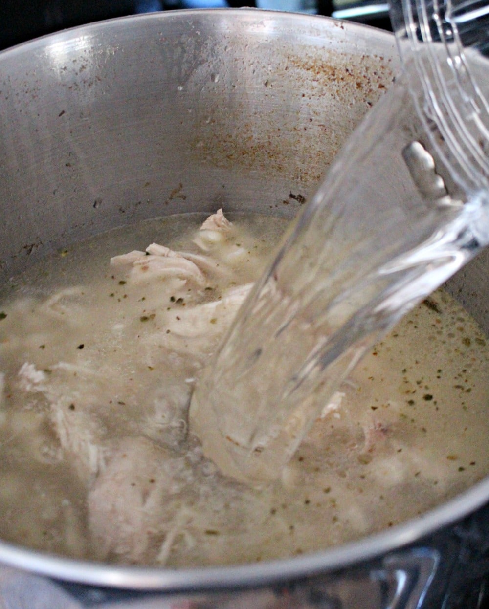 Water pouring into a pot of cooked chicken. 