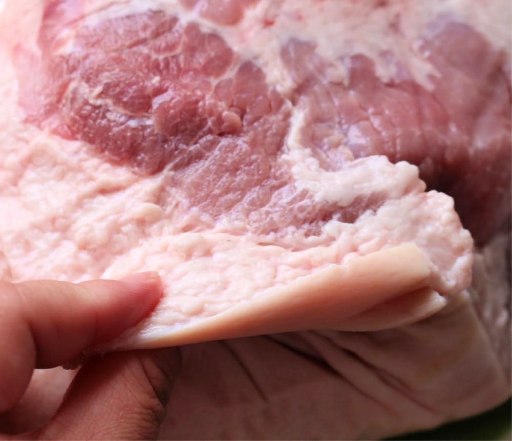 Hand pointing to the fatty layer of the pork shoulder.