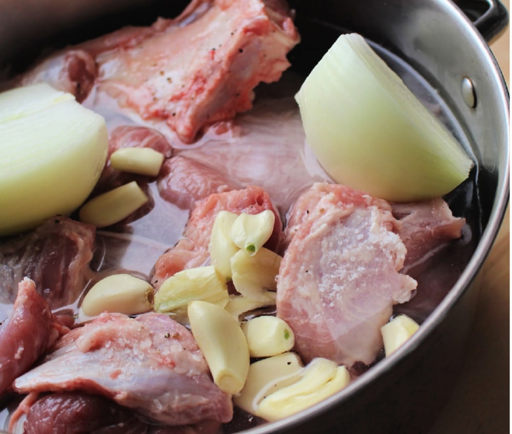 Onion and garlic cloves in the pot of raw pork.