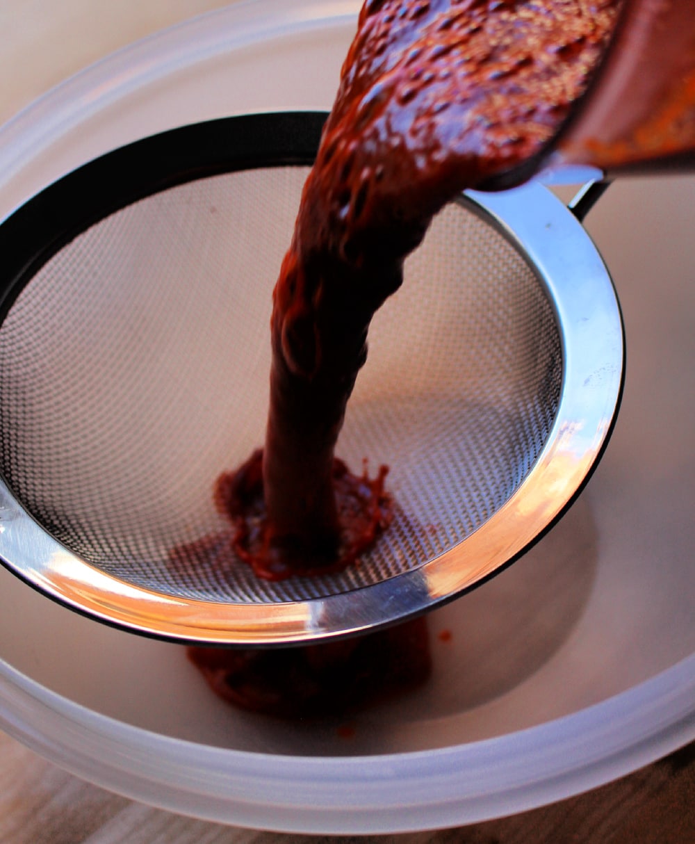Pouring red chile sauce through the strainer.