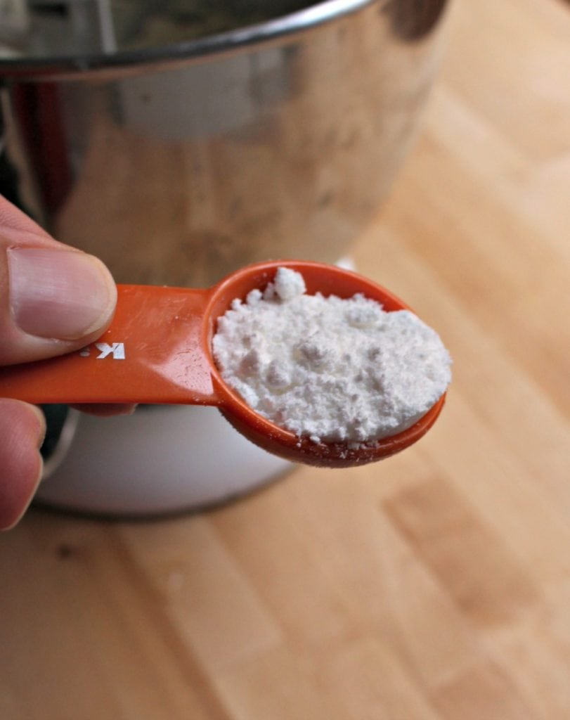 Hand holding orange measuring spoon with baking powder.