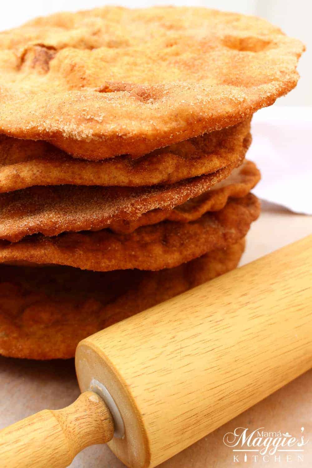 Buñuelos, or Mexican Fritters, stacked up next to a rolling pin.