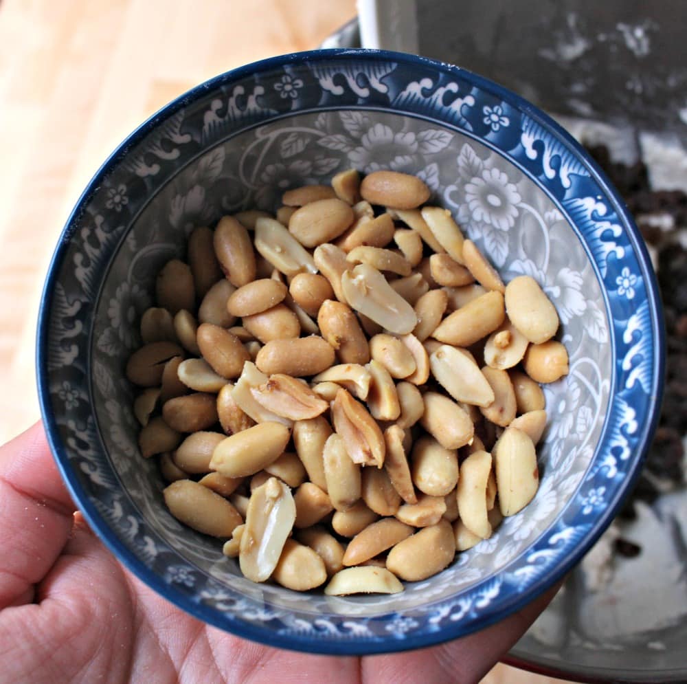 Hand holding a cup cup of peanuts over the masa mixture.