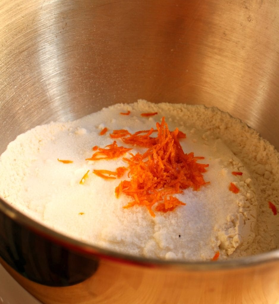 Flour topped with orange zest inside a metal mixing bowl. 