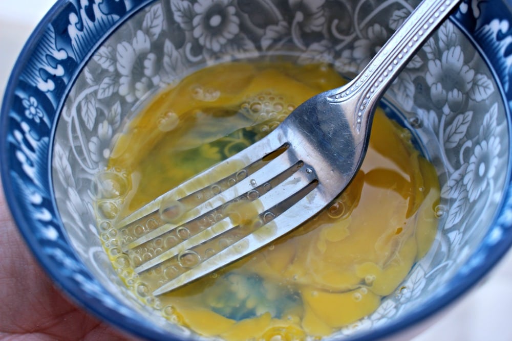 Fork scrambling an egg in a blue bowl.