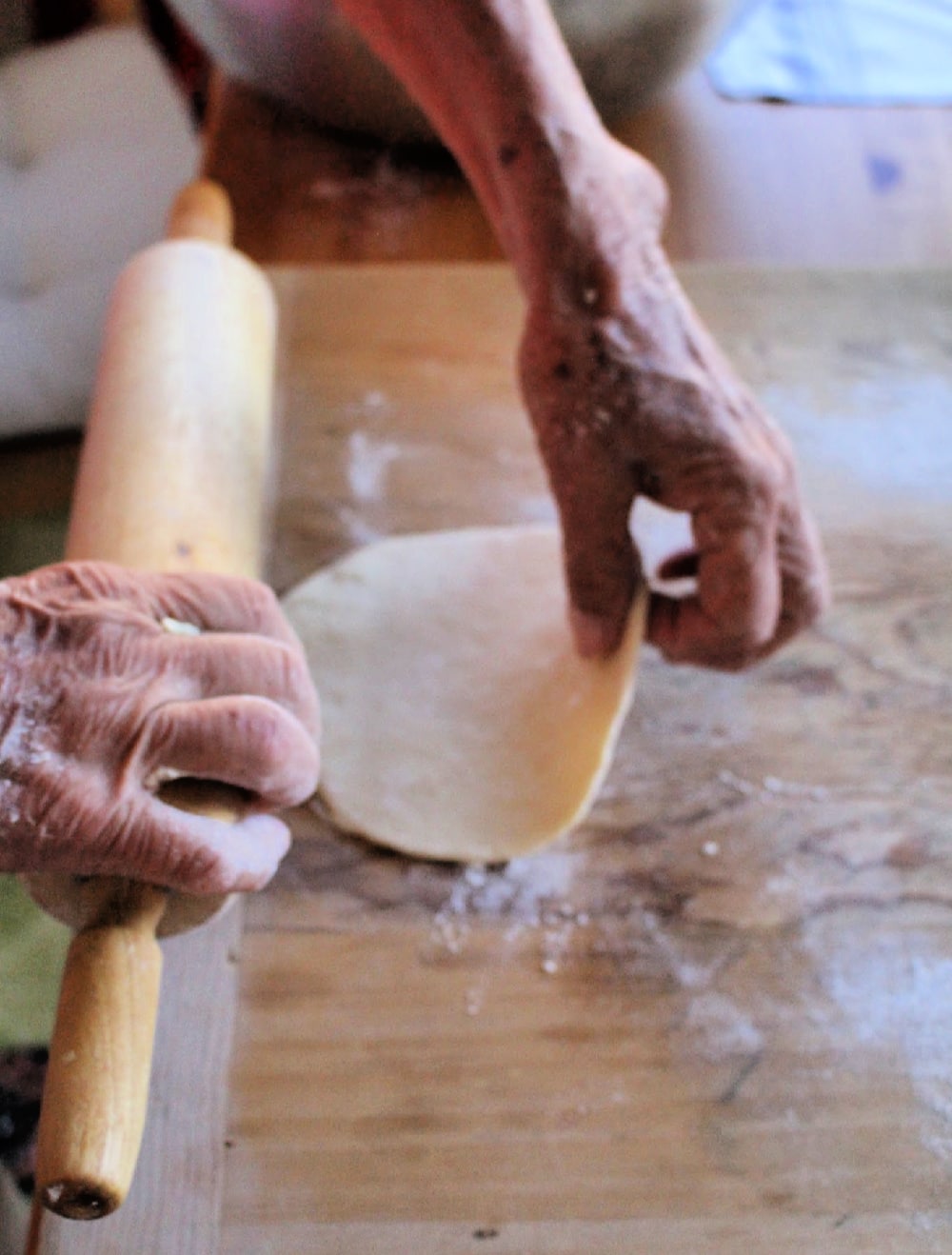 Hand holding a rolling pin and with the other hand flipping the rolled out dough.