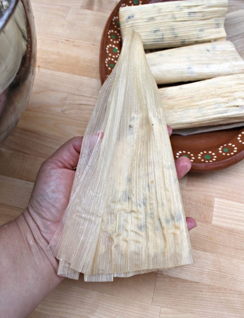 Hand folding tamales over a wooden surface.