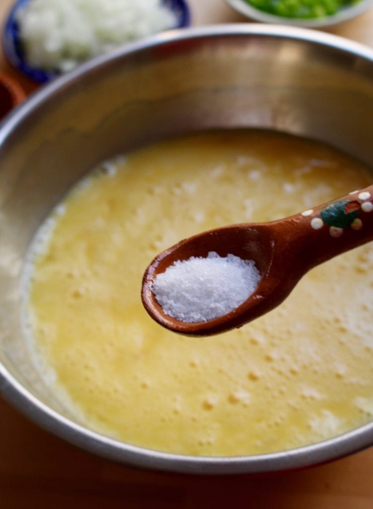 A decorative Mexican spoon holding salt over a bowl of whisked eggs.