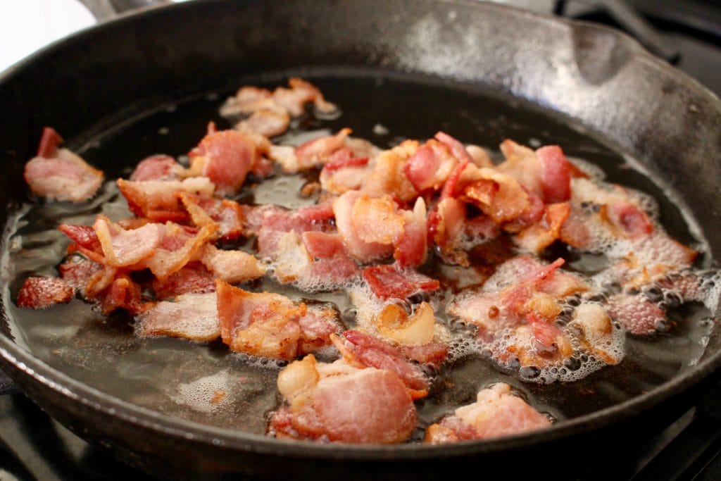 Chopped bacon frying in a black iron skillet.