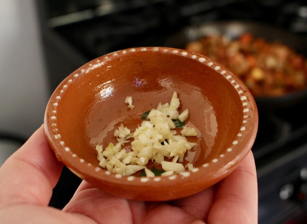 Hand holding a small decorative bowl with diced garlic.
