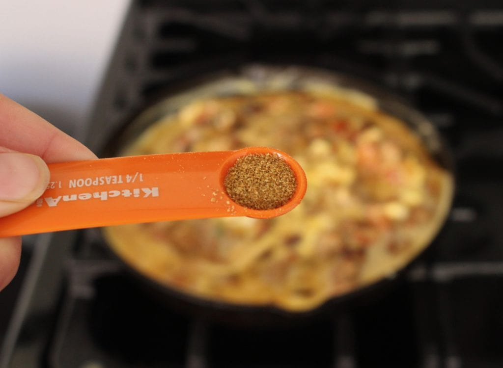 An orange measuring spoon holding ground cumin over a black stove.