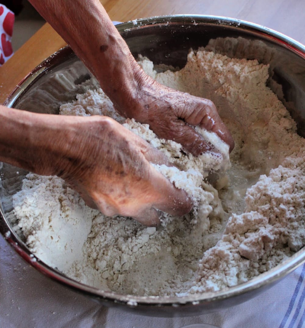 Hands mixing flour in a metal bowl.