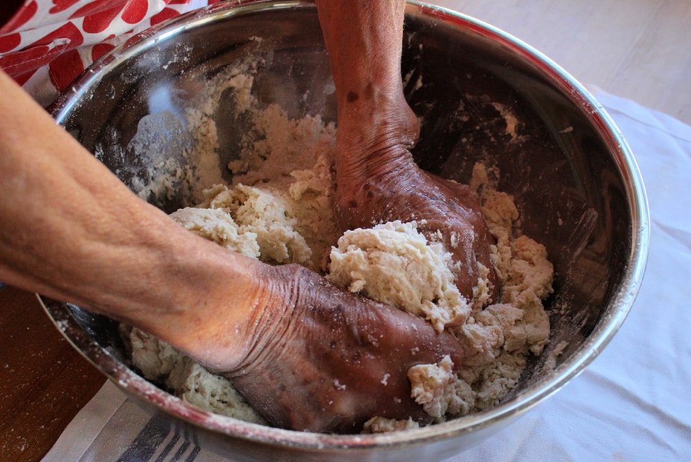 Hands mixing wet dough in a metal bowl.