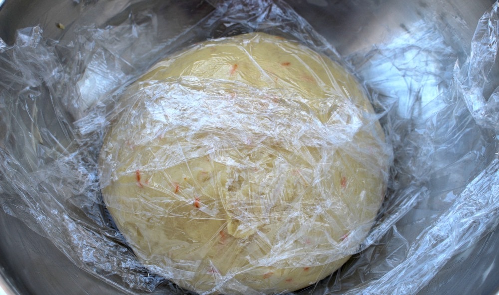 Dough for Rosca de Reyes covered with plastic wrap in a bowl.