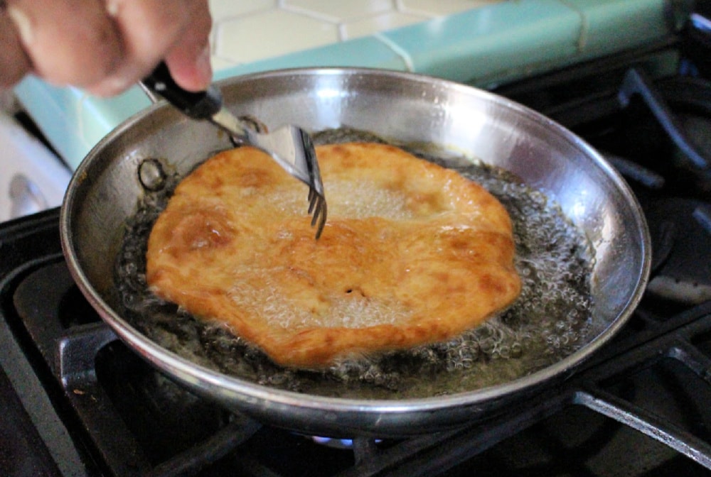 Fork poking the Buñuelos frying in the hot oil pan. 