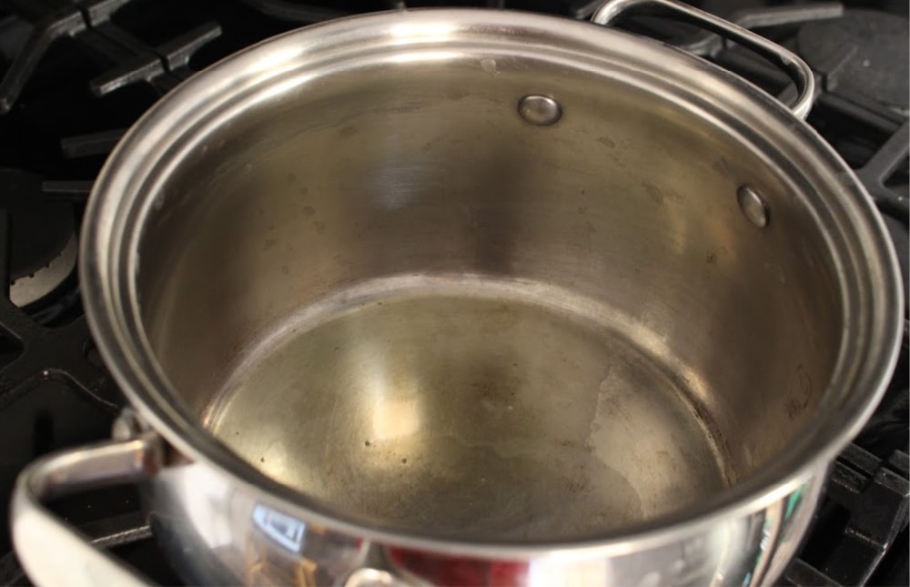 A metal pot with oil in it on a black stove. 