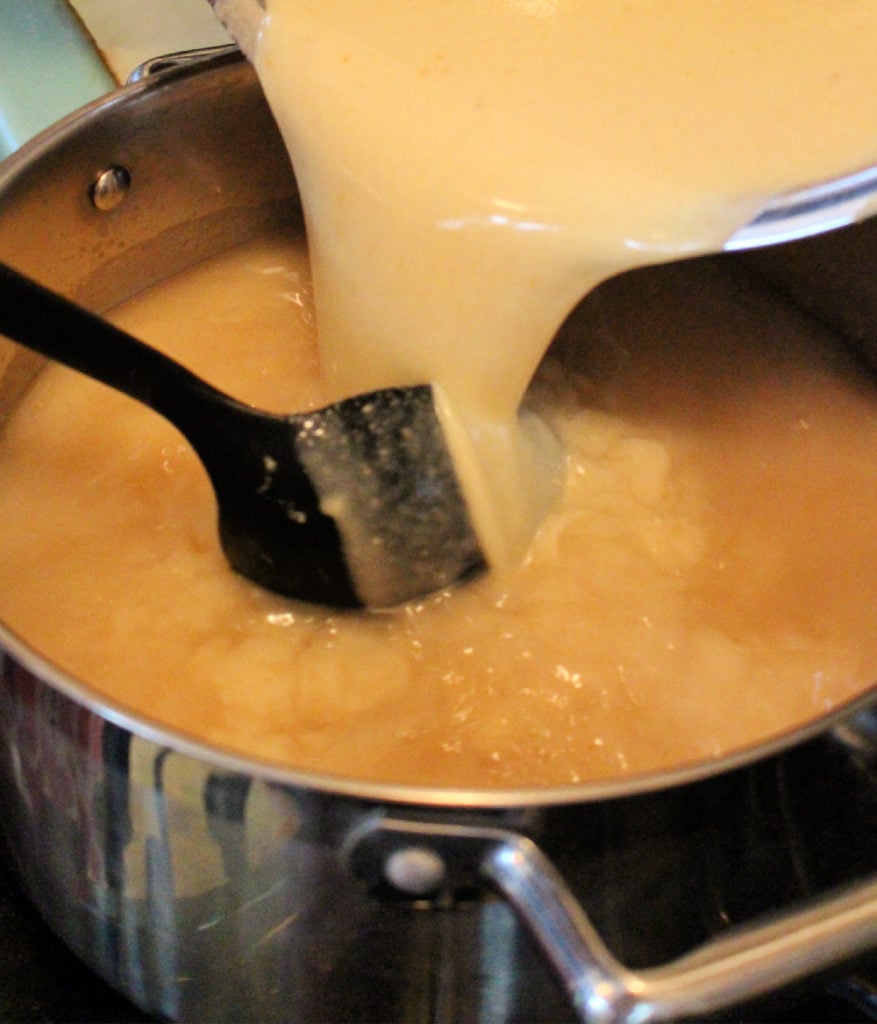 Masa mixture pouring into a pot with a black spoon. 