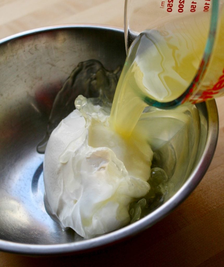 Pineapple juice pouring into a metal bowl with a large dollop of sour cream.