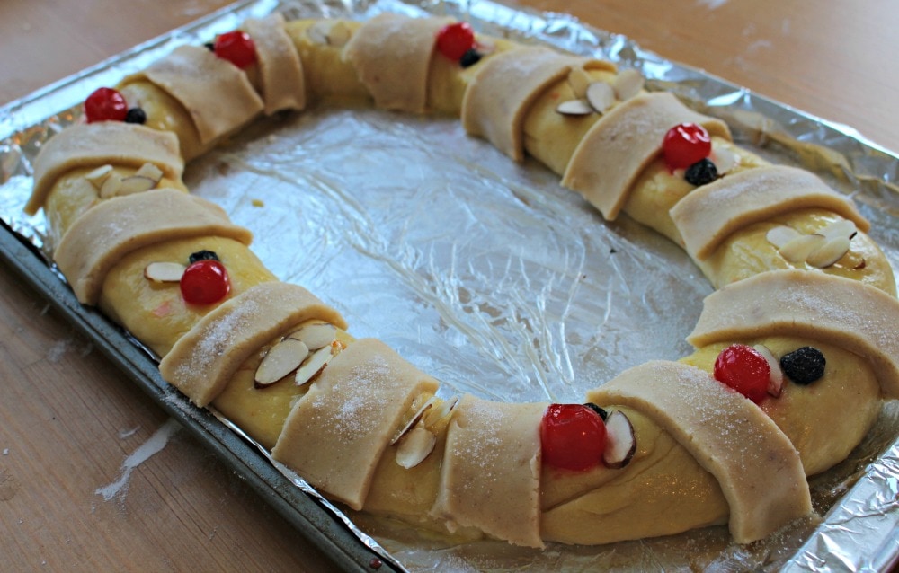 Rosca de Reyes, or King's Cake, on a cookie sheet with toppings ready to be baked.