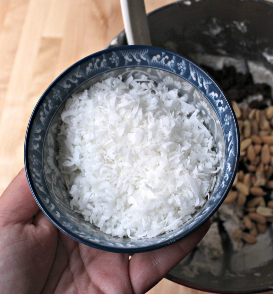 Hand holding a blue cup of shredded coconut over the masa mixture.