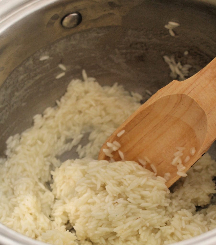 A wooden spoon stirring rice in a metal stock pot. 