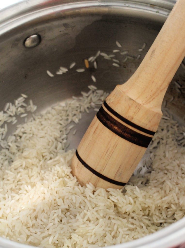 Wooden spoon stirring rice in a metal stock pot.