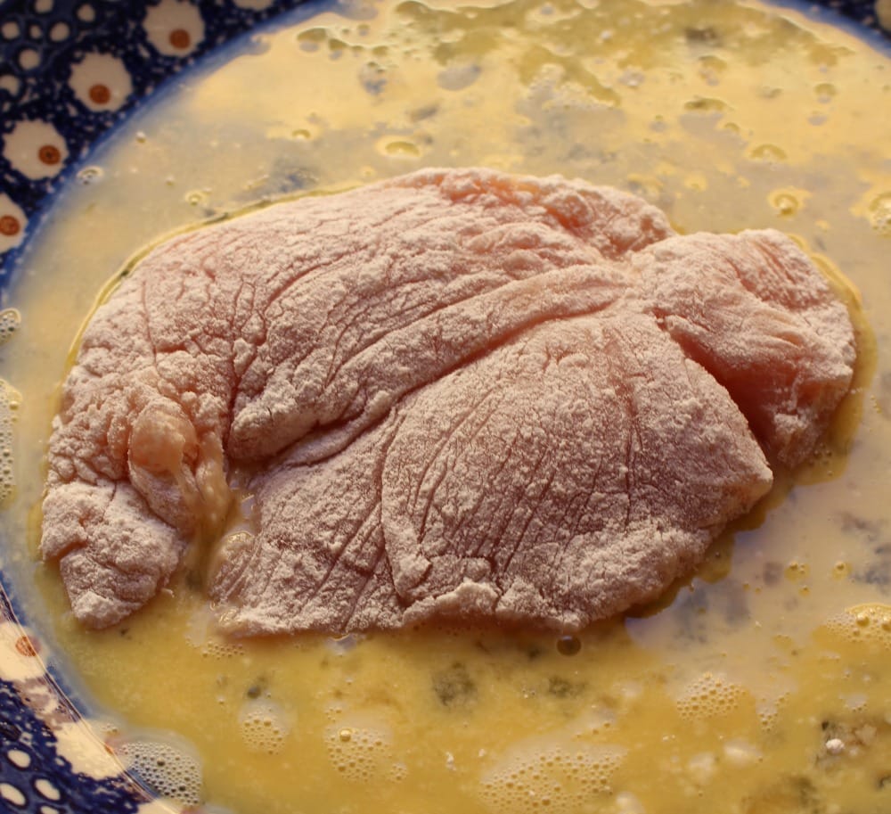 Chicken covered with flour in a plate with eggs.