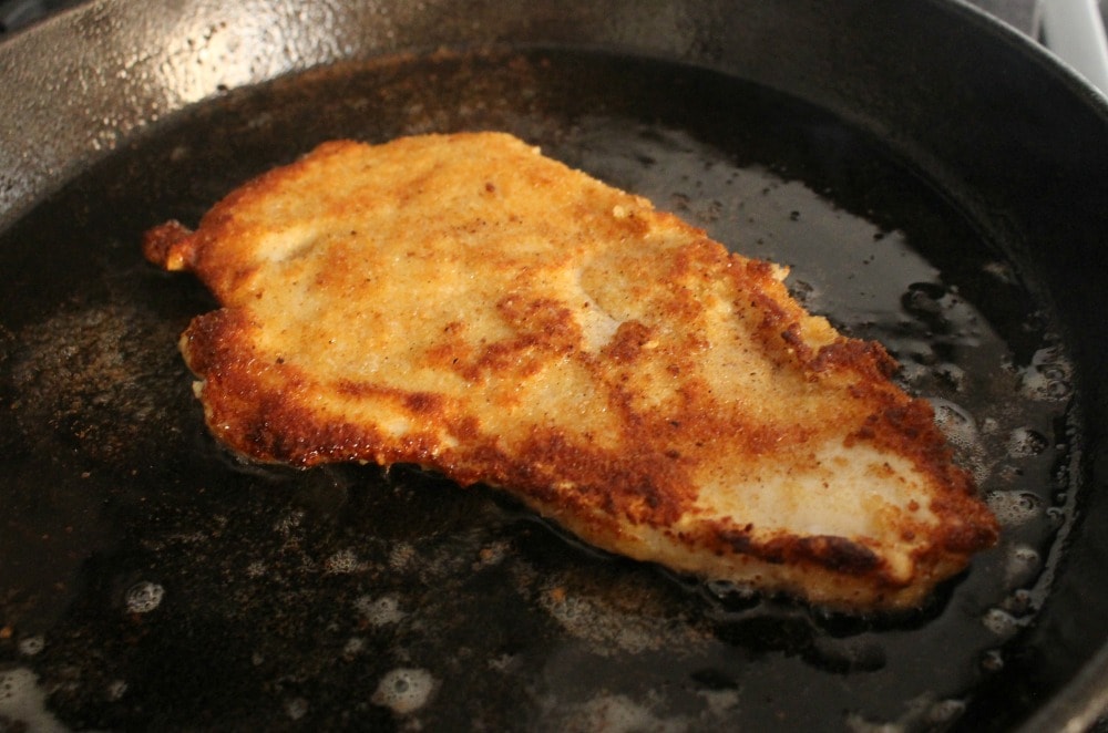 Milanesa de pollo (chicken milanese) frying in a black cast iron skillet.