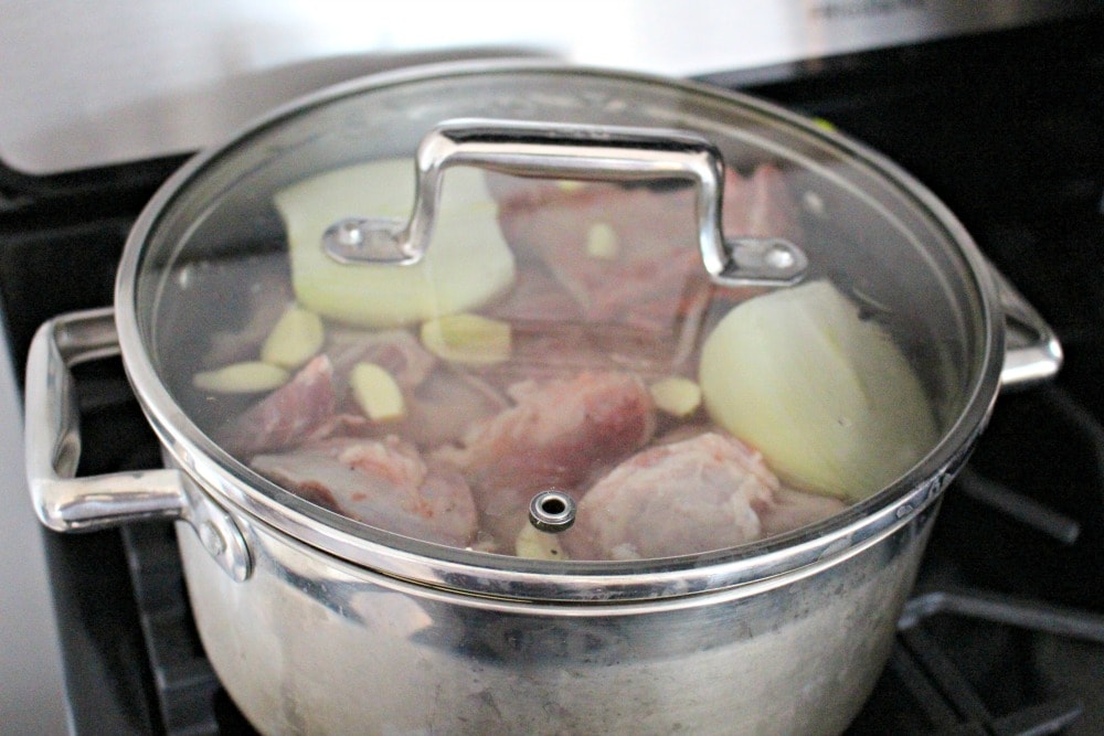 A stock pot cooking pork, onion, garlic, and filled with water.