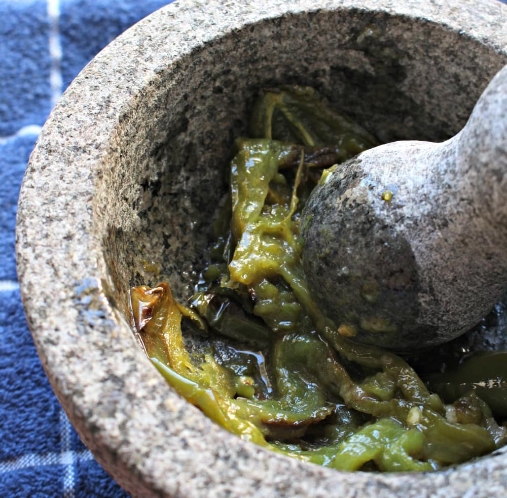 The pestle mashing up the jalapeno in a molcajete.