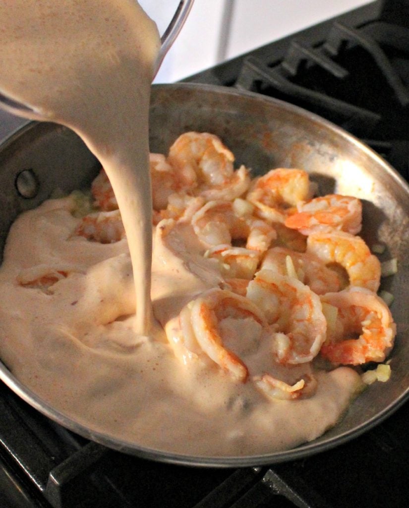 Chipotle cream sauce pouring into a skillet with cooked shrimp.