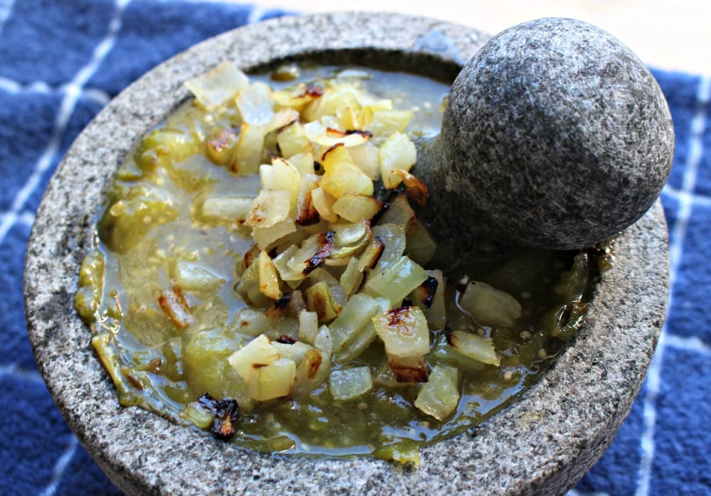 Roasted diced onion in a molcajete salsa verde sitting on a blue towel.