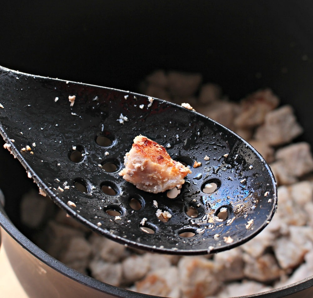 A black spatula holding up a seared piece of pork over the pot. 