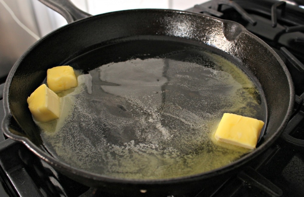 Two tabs of butter melting in a black cast iron skillet.