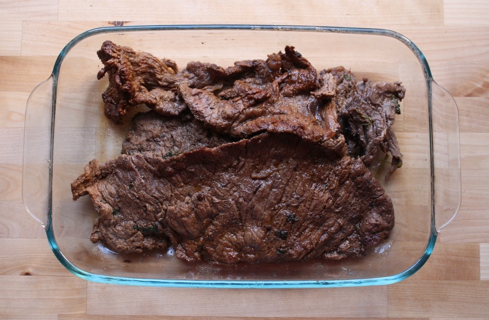 Grilled steak cooling in a glass baking dish.