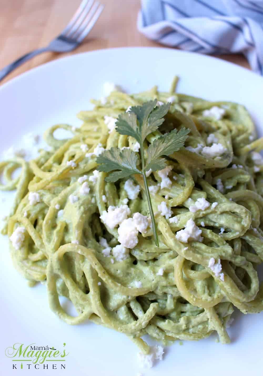 Espagueti Verde on a white plate topped with a cilantro leaf and crumbled cheese.