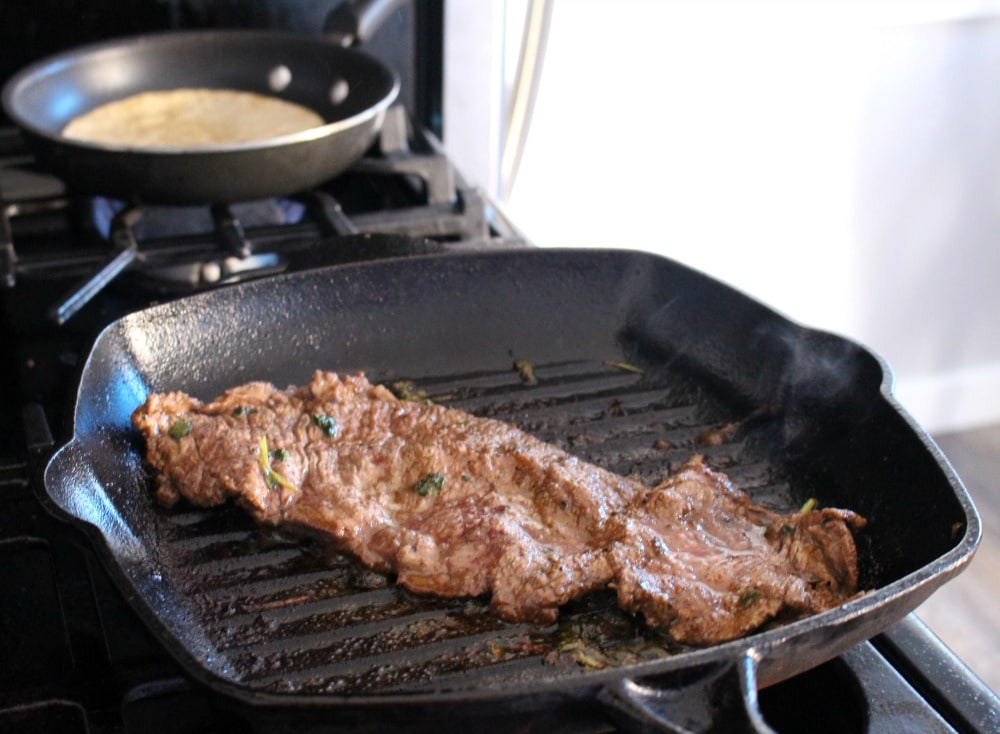 Grilling steak on a black cast iron grill skillet next to a cooking tortilla.