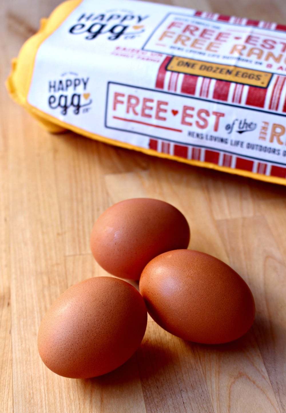 Three eggs with a carton of Happy Egg in the background.