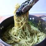 Tongs lifting spaghetti that has been mixed with the creamy poblano sauce.