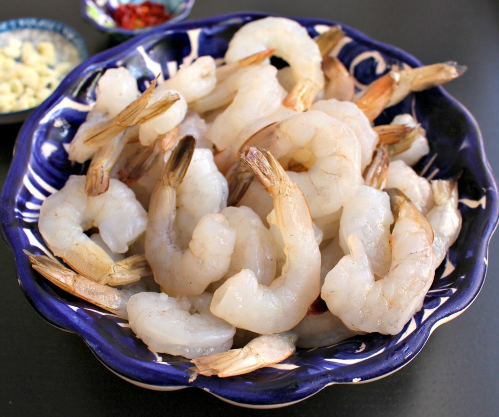 Peeled shrimp with their tails still on in a decorative blue bowl.
