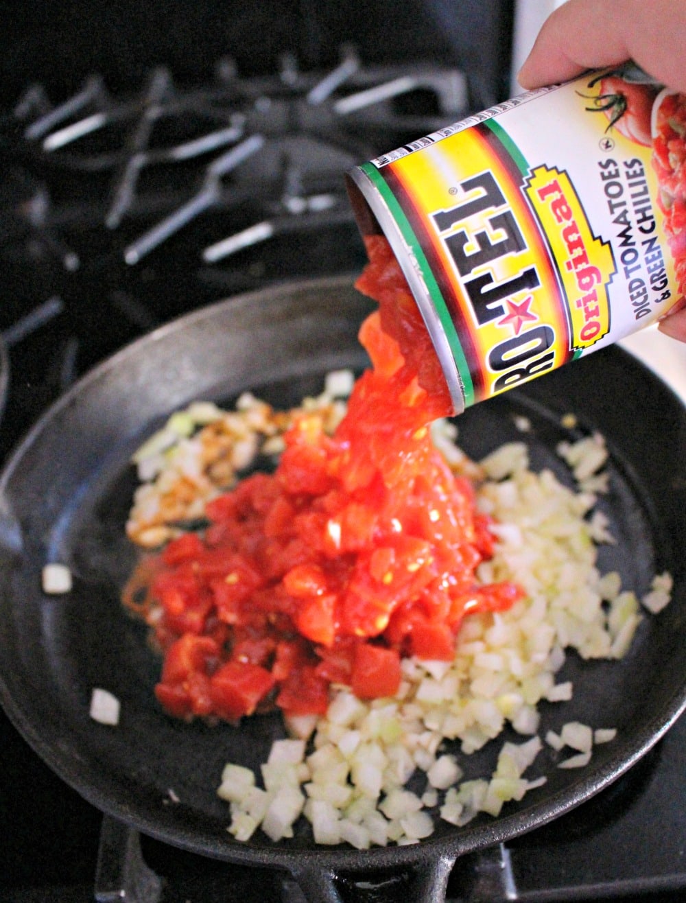 A hand pouring the tomatoes from a Ro*tel can into a skillet.