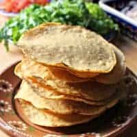 A large stack of tostadas on a decorative Mexican clay plate.
