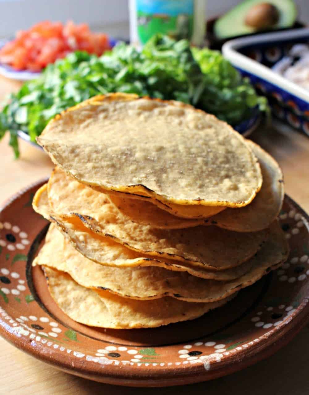 A large stack of tostadas on a decorative Mexican clay plate.